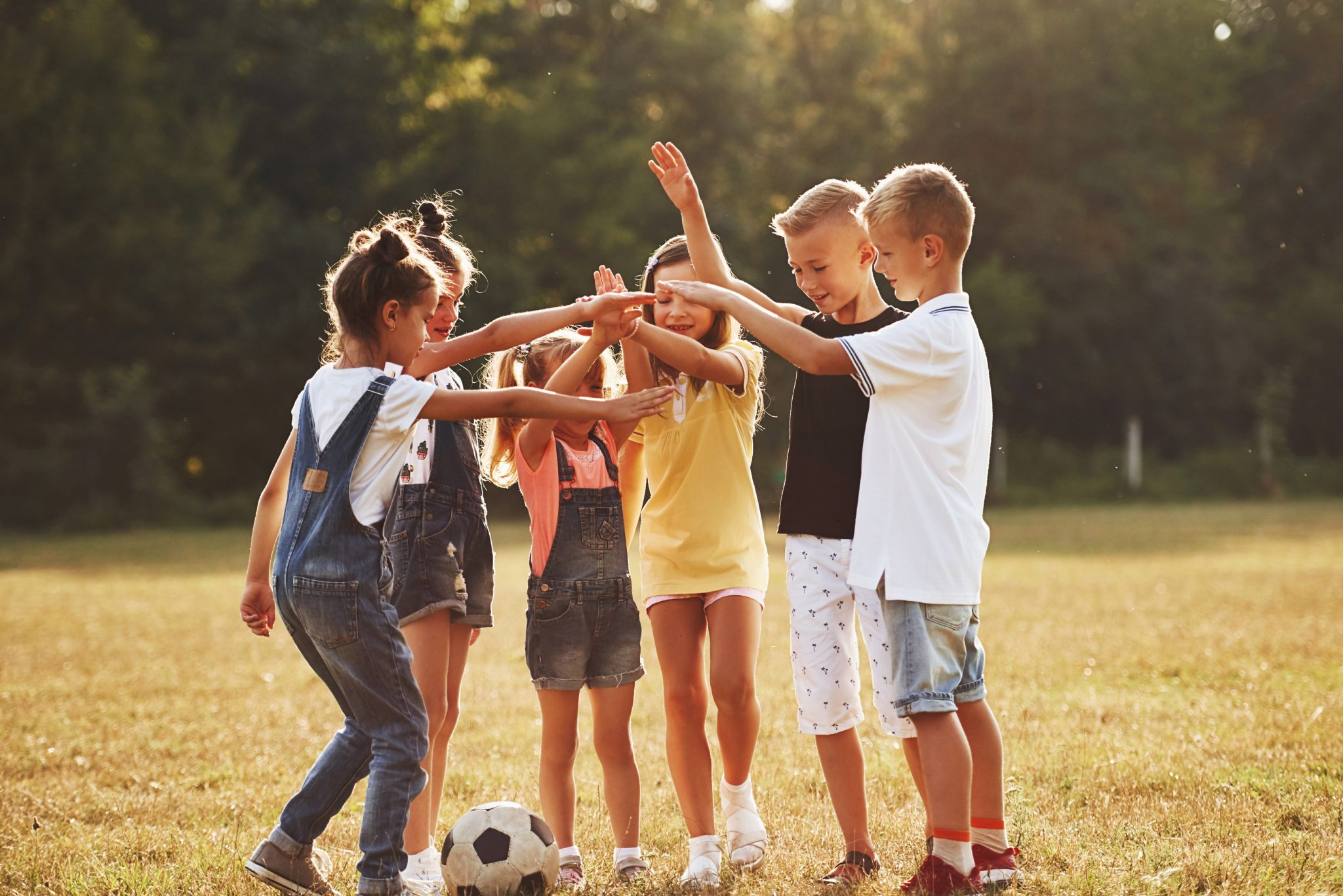 Ready for the game. Young sportive kids with soccer ball stands together in the field at sunny day.